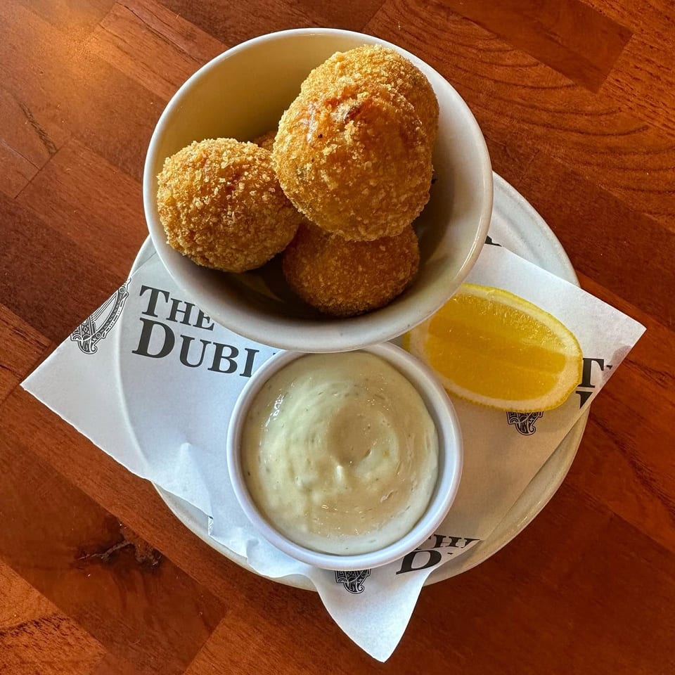 Three golden fried croquettes in a bowl with dipping sauce and a lemon wedge on a wooden table.