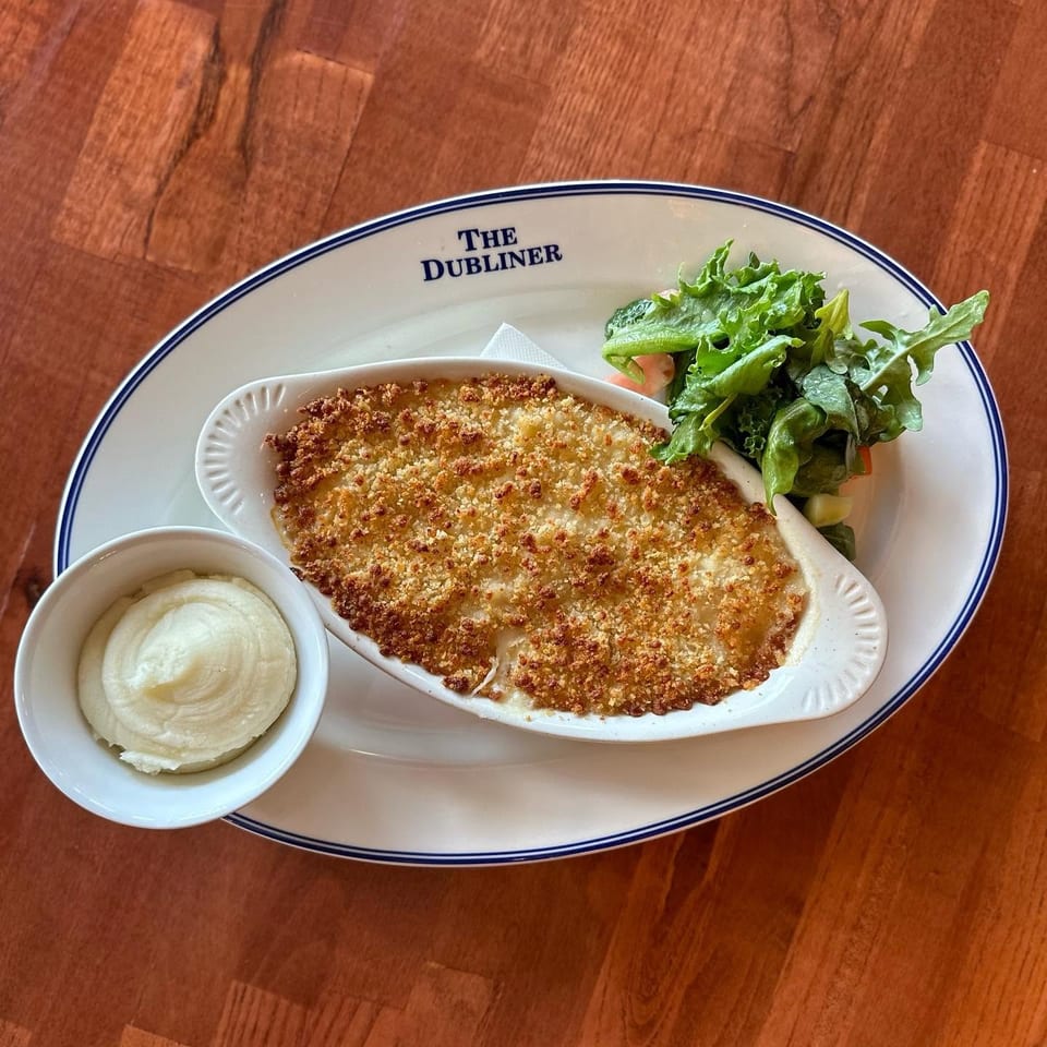 Breaded baked entrée served with green salad and mashed potatoes on a branded The Dubliner plate.